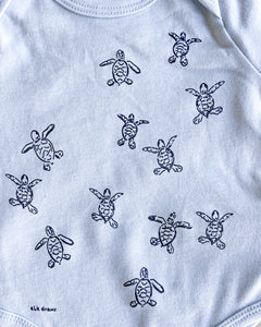 Baby blue organic cotton onesie with turtle hatchlings on it.