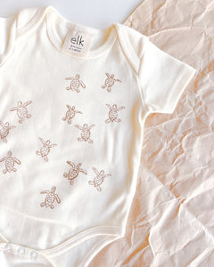 Baby ecru organic cotton onesie with turtle hatchlings on it.