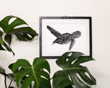 Load image into Gallery viewer, Green sea turtle print hanging on white wall behind monstera