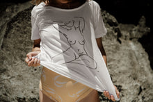 Load image into Gallery viewer, Girl on beach in white organic cotton tshirt wth nude female form line art design on front by elk draws