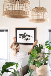 women hanging orca print in living area in bright modern house with monstera
