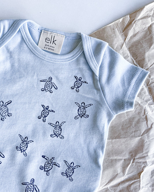 Baby blue organic cotton onesie with turtle hatchlings on it.