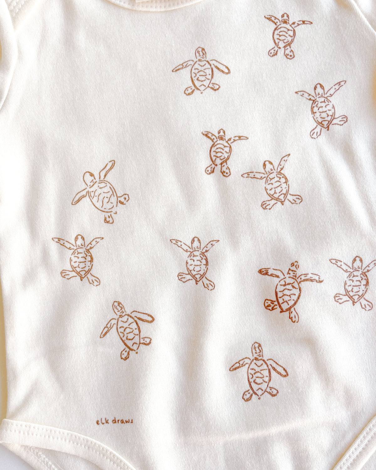 Baby ecru organic cotton onesie with turtle hatchlings on it.