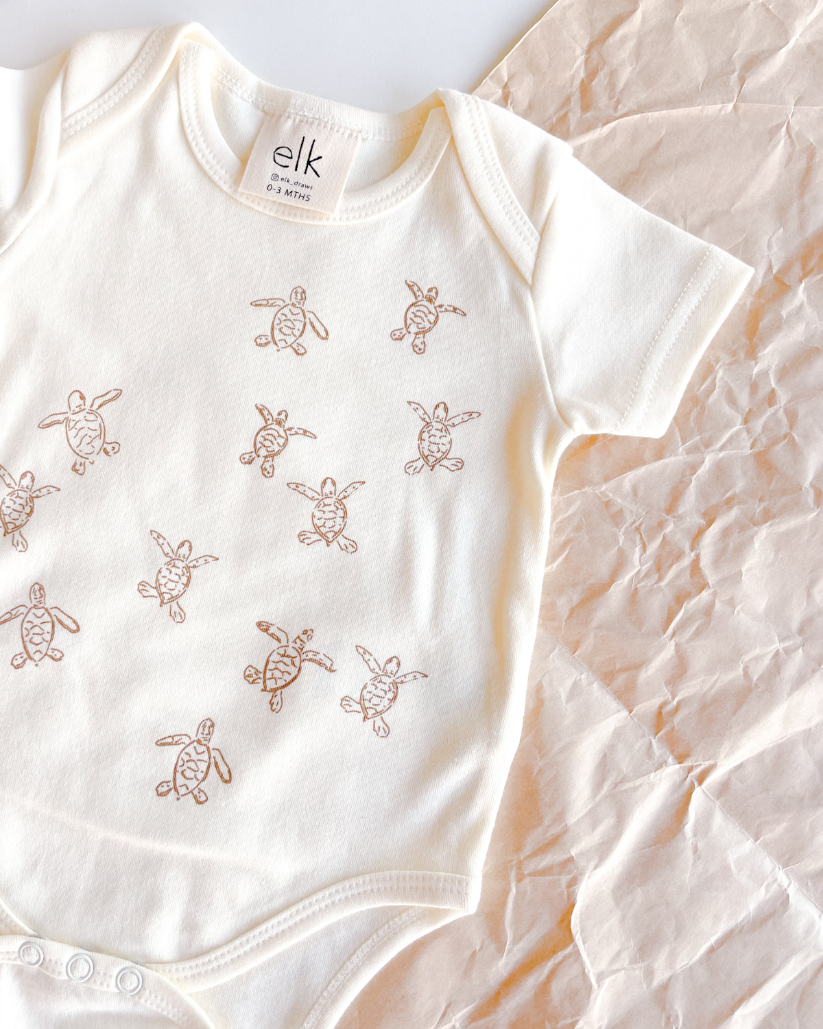 Baby ecru organic cotton onesie with turtle hatchlings on it.