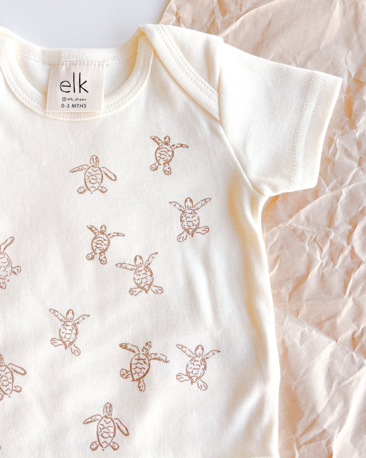 Baby ecru organic cotton onesie with turtle hatchlings on it.