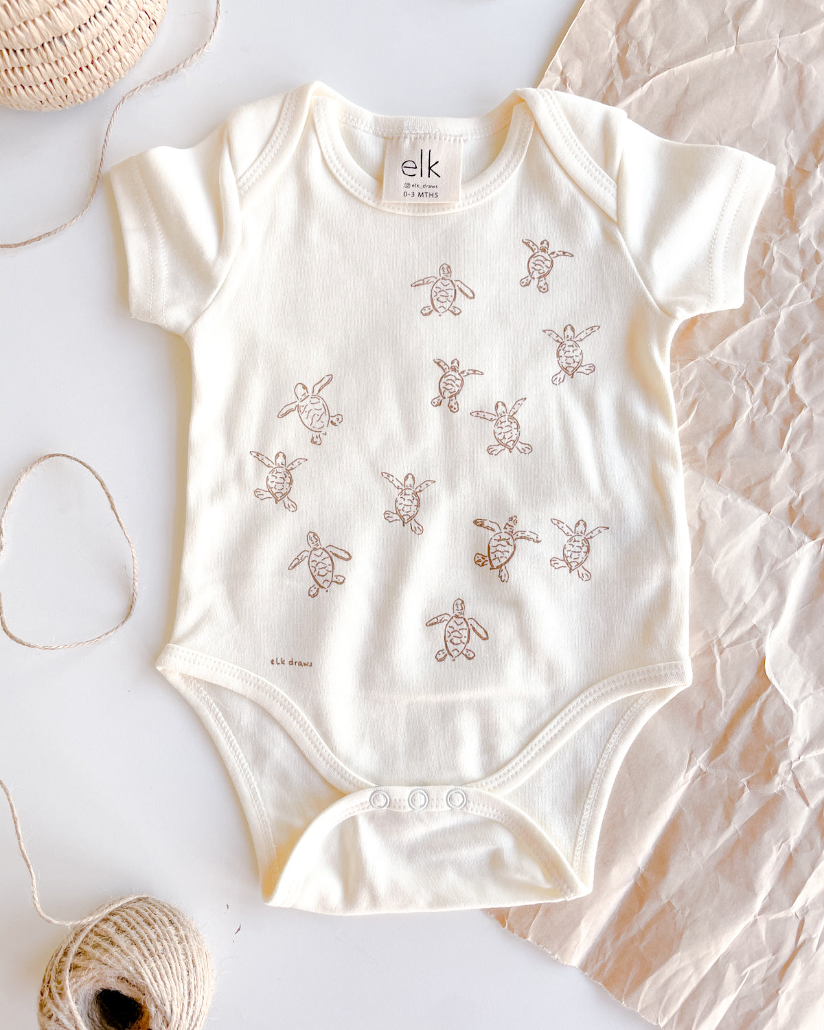 Baby ecru organic cotton onesie with turtle hatchlings on it.