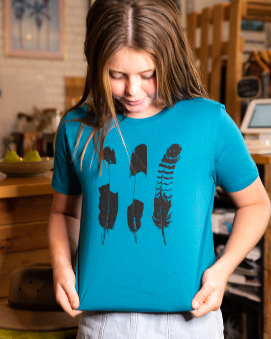 Young girl wearing elk draws blue organic cotton tshirt with three feathers on it.