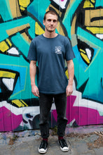 Load image into Gallery viewer, Man standing next to graffiti with blue organic cotton tshirt with covid squid design by elk draws